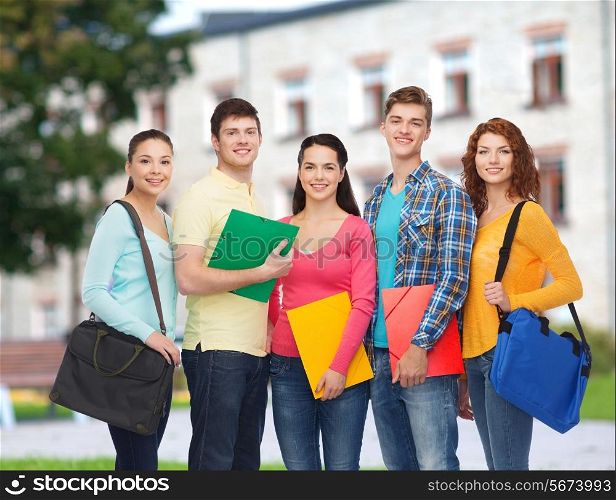 friendship, school, education and people concept - group of smiling teenagers with folders and school bags over campus background