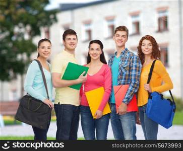 friendship, school, education and people concept - group of smiling teenagers with folders and school bags over campus background