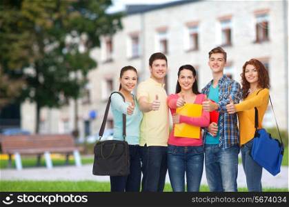 friendship, school, education, gesture and people concept - group of smiling teenagers with folders and school bags showing thumbs up over campus background