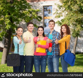 friendship, school, education, gesture and people concept - group of smiling teenagers with folders and school bags showing thumbs up over campus background