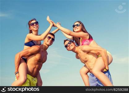 friendship, sea, gesture, holidays and people concept - group of smiling friends wearing swimwear having fun and making high five on beach