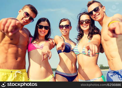 friendship, sea, holidays, gesture and people concept - group of smiling friends wearing swimwear and sunglasses pointing on you on beach