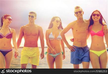 friendship, sea, summer vacation, holidays and people concept - group of smiling friends wearing swimwear and sunglasses walking on beach. smiling friends in sunglasses on summer beach