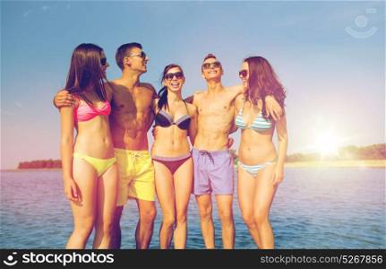 friendship, sea, summer vacation, holidays and people concept - group of smiling friends wearing swimwear and sunglasses talking and laughing on beach. smiling friends in sunglasses on summer beach