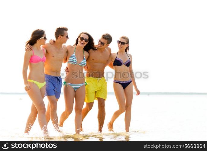 friendship, sea, summer vacation, holidays and people concept - group of smiling friends wearing swimwear and sunglasses walking on beach