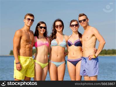 friendship, sea, summer vacation, holidays and people concept - group of smiling friends wearing swimwear and sunglasses on beach