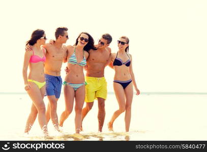 friendship, sea, summer vacation, holidays and people concept - group of smiling friends wearing swimwear and sunglasses walking on beach