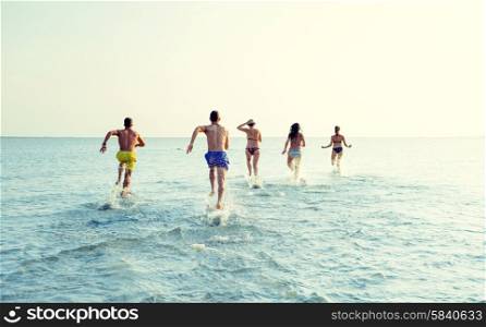 friendship, sea, summer vacation, holidays and people concept - group of smiling friends in swimwear running on beach from back
