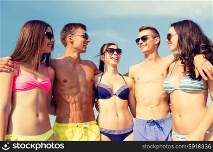 friendship, sea, summer vacation, holidays and people concept - group of smiling friends wearing swimwear and sunglasses talking and laughing on beach