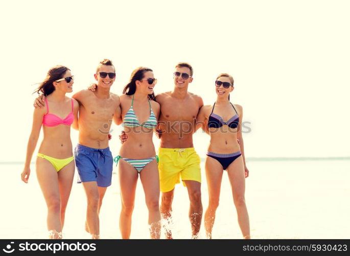 friendship, sea, summer vacation, holidays and people concept - group of smiling friends wearing swimwear and sunglasses walking on beach