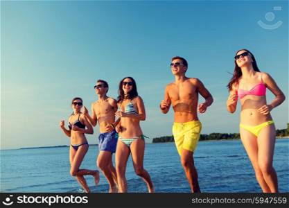 friendship, sea, summer vacation, holidays and people concept - group of smiling friends wearing swimwear and sunglasses running on beach