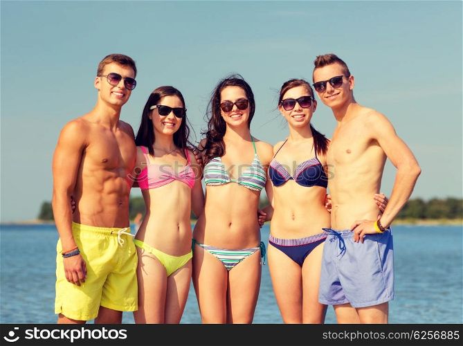 friendship, sea, summer vacation, holidays and people concept - group of smiling friends wearing swimwear and sunglasses on beach