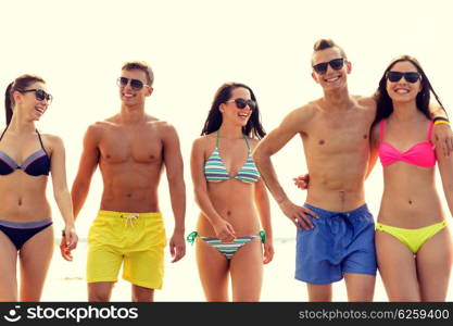 friendship, sea, summer vacation, holidays and people concept - group of smiling friends wearing swimwear and sunglasses walking on beach