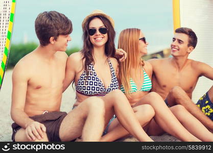 friendship, sea, summer vacation, water sport and people concept - group of smiling friends wearing swimwear and sunglasses with surfboards on beach