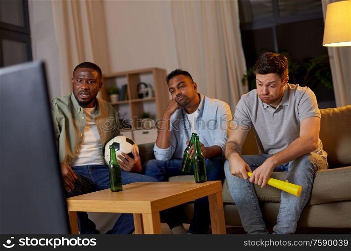friendship, sports and entertainment concept - disappointed male friends with soccer ball and vuvuzela watching football game at home. sad friends with beer watching soccer at home