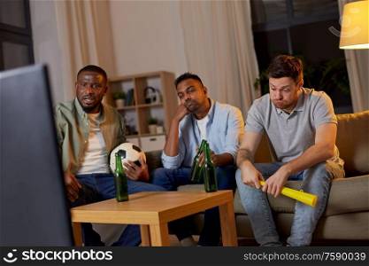 friendship, sports and entertainment concept - disappointed male friends with soccer ball and vuvuzela watching football game at home. sad friends with beer watching soccer at home