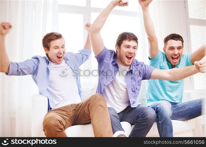 friendship, sports and entertainment concept - happy male friends supporting football team at home