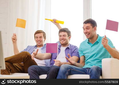 friendship, sports and entertainment concept - happy male friends with flags and vuvuzela supporting football team at home