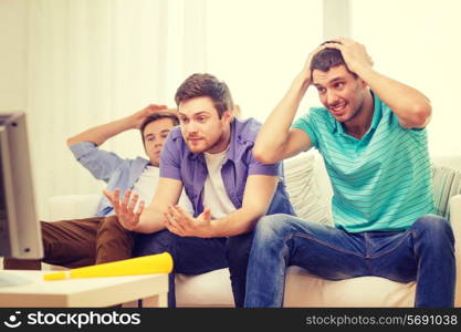 friendship, sports and entertainment concept - sad male friends with vuvuzela watching sports on tv at home