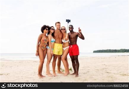 friendship, summer holidays and people concept - group of happy friends taking picture by smartphone on selfie stick on beach. happy friends taking selfie on summer beach