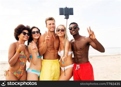 friendship, summer holidays and people concept - group of happy friends taking picture by smartphone on selfie stick on beach. happy friends taking selfie on summer beach