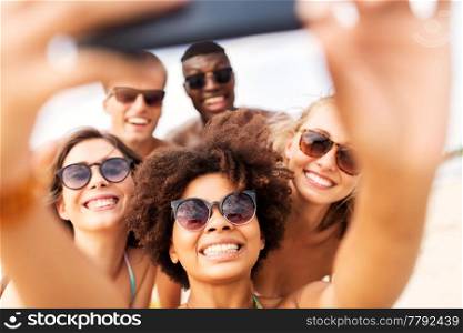 friendship, summer holidays and people concept - group of happy friends taking picture by smartphone on beach. happy friends taking selfie on summer beach