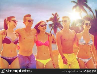 friendship, summer holidays and people concept - group of smiling friends wearing swimwear and sunglasses walking over exotic tropical beach with palm trees background. smiling friends in sunglasses on summer beach