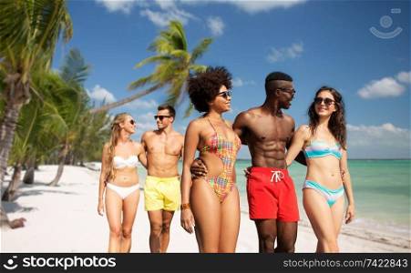 friendship, summer holidays and vacation concept - happy friends walking along tropical beach of french polynesia background. happy friends walking along summer beach
