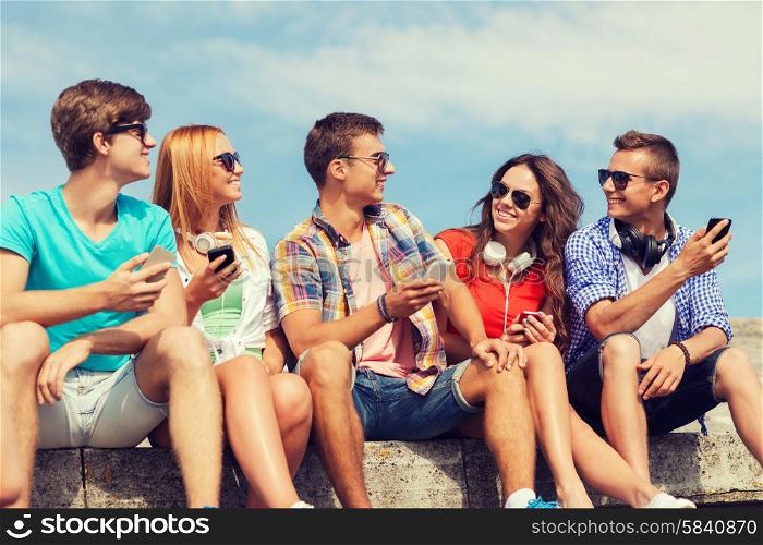 friendship, summer, technology and people concept - group of smiling friends with smartphones and headphones outdoors