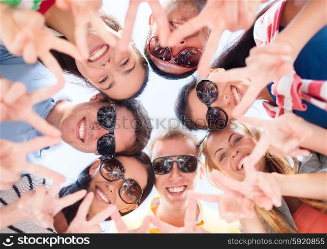 friendship, summer vacation, holidays and people concept - group of smiling friends showing victory gesture in circle over blue sky