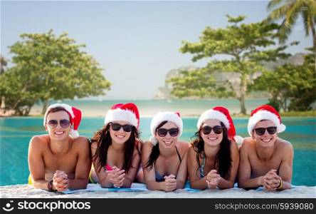 friendship, summer vacation, holidays, travel and people concept - group of friends in santa helper hats on beach