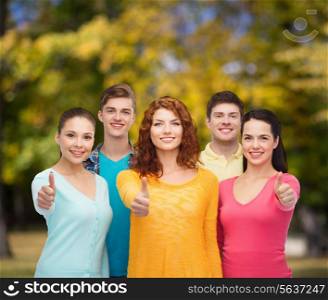 friendship, summer vacation, nature and people concept - group of smiling teenagers showing thumbs up over green park background