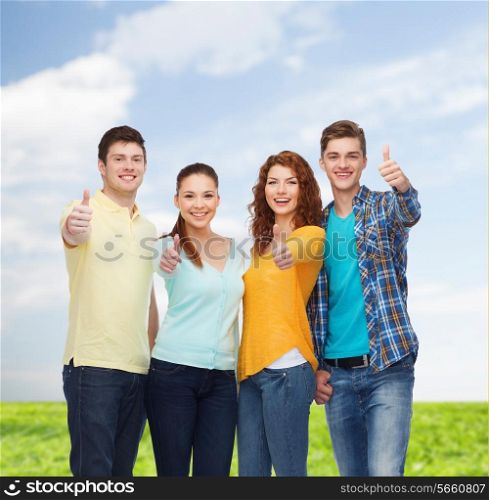 friendship, summer vacation, nature and people concept - group of smiling teenagers showing thumbs up over blue sky and grass background