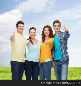 friendship, summer vacation, nature and people concept - group of smiling teenagers showing thumbs up over blue sky and grass background