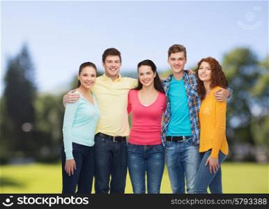 friendship, summer vacation, nature and people concept - group of smiling teenagers standing and embracing over green park background