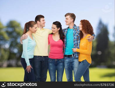 friendship, summer vacation, nature and people concept - group of smiling teenagers standing and embracing over green park background