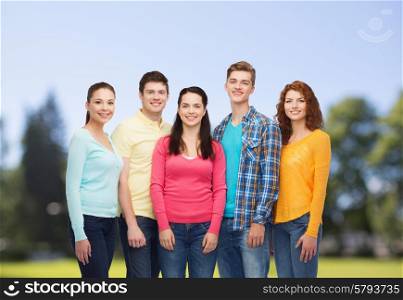 friendship, summer vacation, nature and people concept - group of smiling teenagers standing over green park background