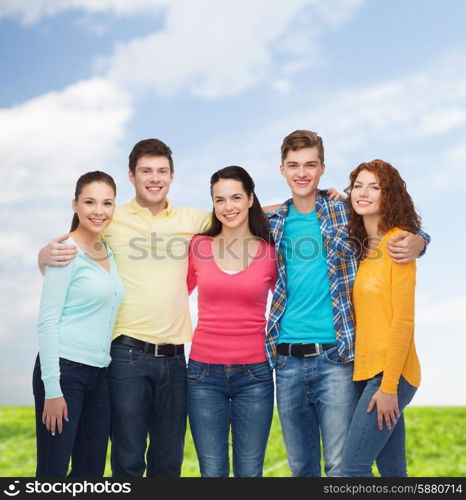 friendship, summer vacation, nature and people concept - group of smiling teenagers standing over blue sky and grass background