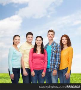 friendship, summer vacation, nature and people concept - group of smiling teenagers standing over blue sky and grass background