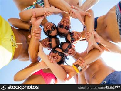 friendship, summer vacation, teamwork and people concept - group of smiling friends wearing swimwear standing in circle over blue sky holding hands connected to each other