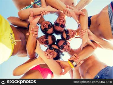 friendship, summer vacation, teamwork and people concept - group of smiling friends wearing swimwear standing in circle over blue sky holding hands connected to each other