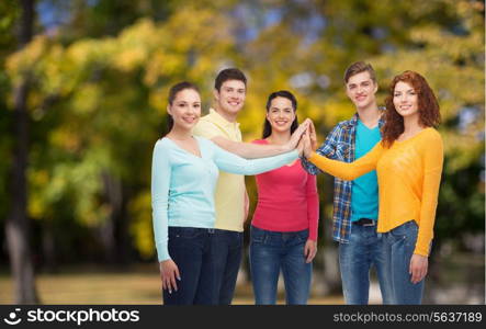 friendship, summer vacation, teamwork, gesture and people concept - group of smiling teenagers making high five over green park background