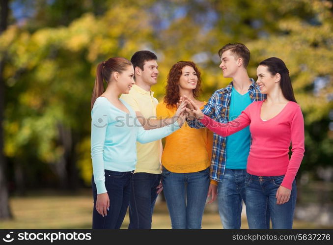 friendship, summer vacation, teamwork, gesture and people concept - group of smiling teenagers making high five over green park background