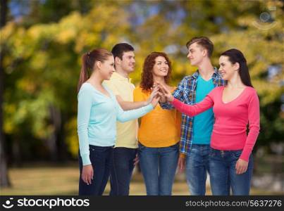 friendship, summer vacation, teamwork, gesture and people concept - group of smiling teenagers making high five over green park background