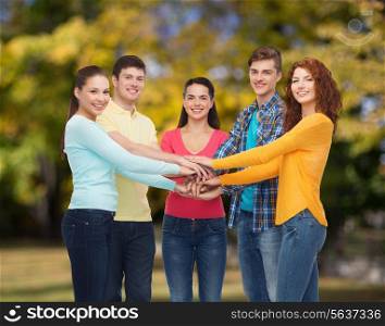 friendship, summer vacation, teamwork, gesture and people concept - group of smiling teenagers putting hand on top of each other over green park background