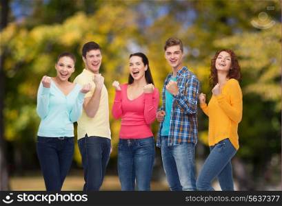 friendship, summer vacation, teamwork, gesture and people concept - group of smiling teenagers showing triumph gesture over green park background