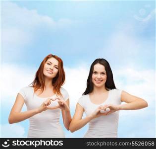 friendship, t-shirt design and happy people concept - two smiling girls in white blank t-shirts showing heart with hands