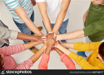 friendship, teamwork and people concept - group of international men and women with hands on top of each other