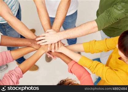 friendship, teamwork and people concept - group of international men and women with hands on top of each other