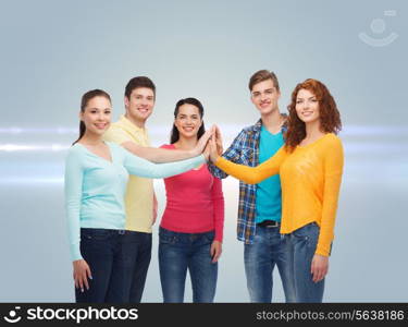 friendship, teamwork, gesture and people concept - group of smiling teenagers making high five over gray background with laser light